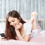 Young girl with smartphon lying on the bed